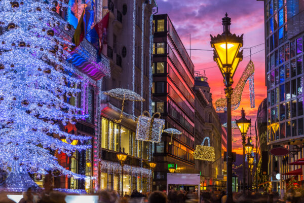 Budapest, Ungheria - Albero di Natale scintillante e turisti nella trafficata via Vaci, la famosa via dello shopping di Budapest nel periodo natalizio con negozi e un bel cielo al tramonto